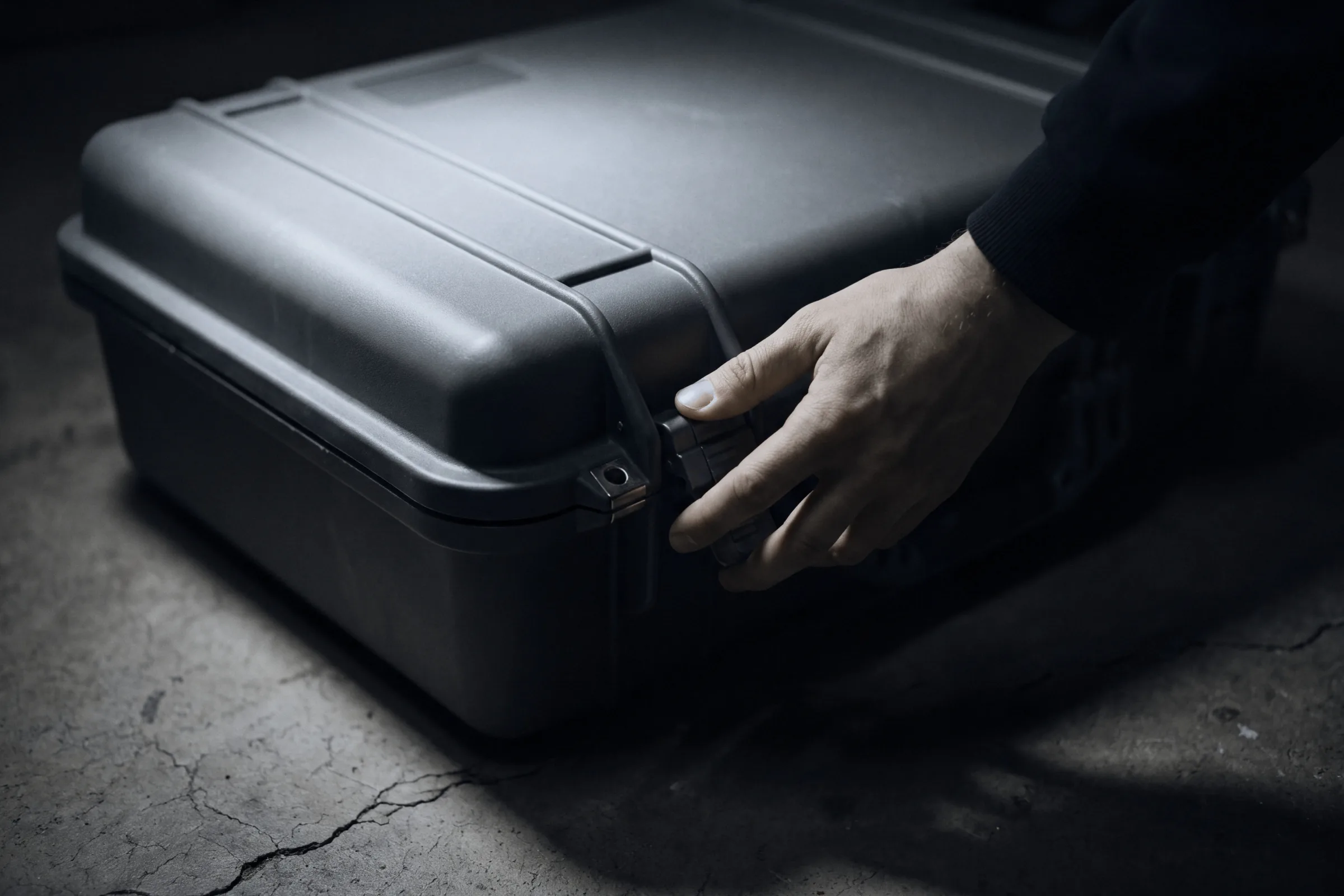 A hand opening a hard case on a concrete floor