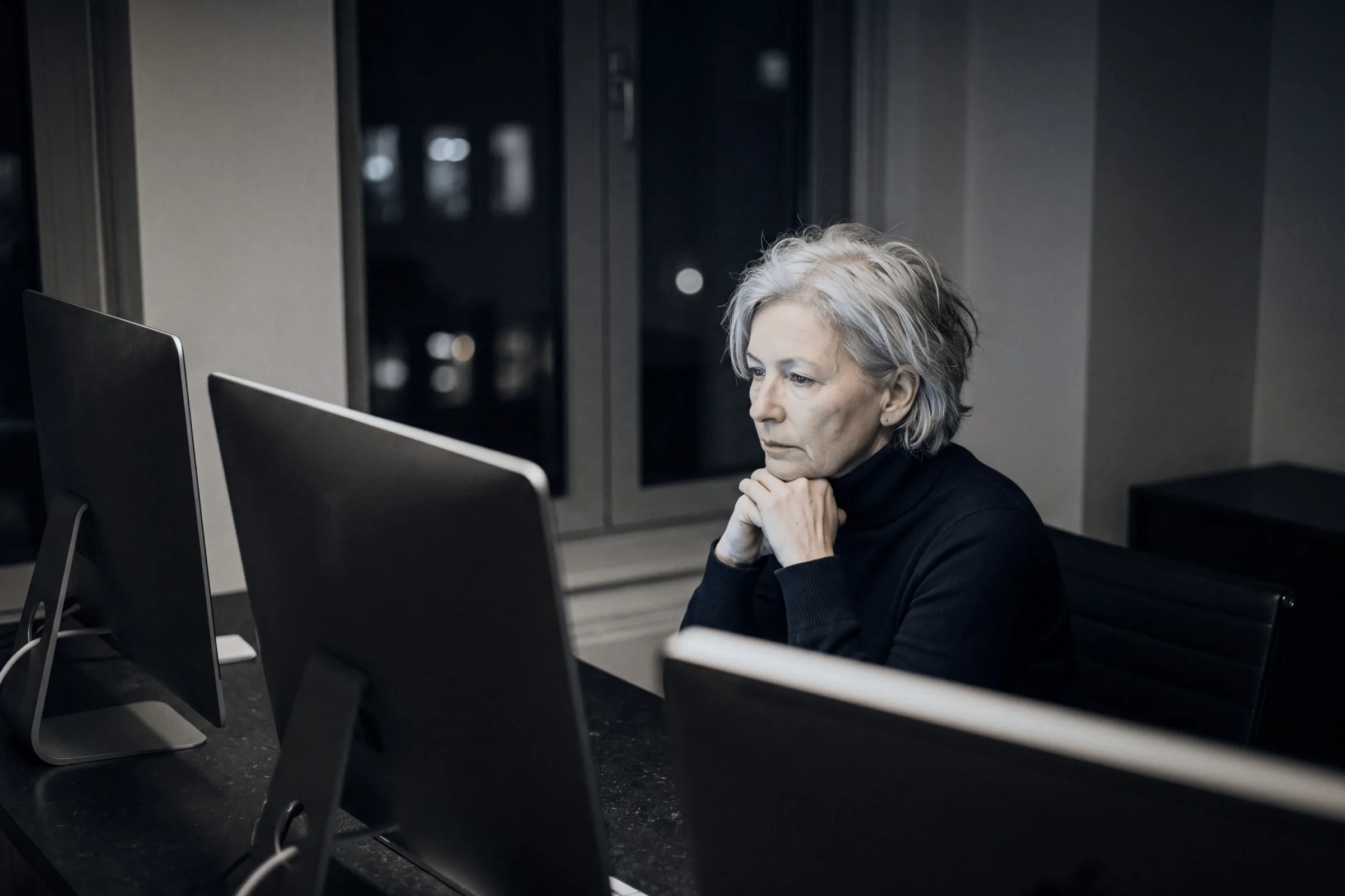 An analyst at her desk in the evening, two screens in front of her