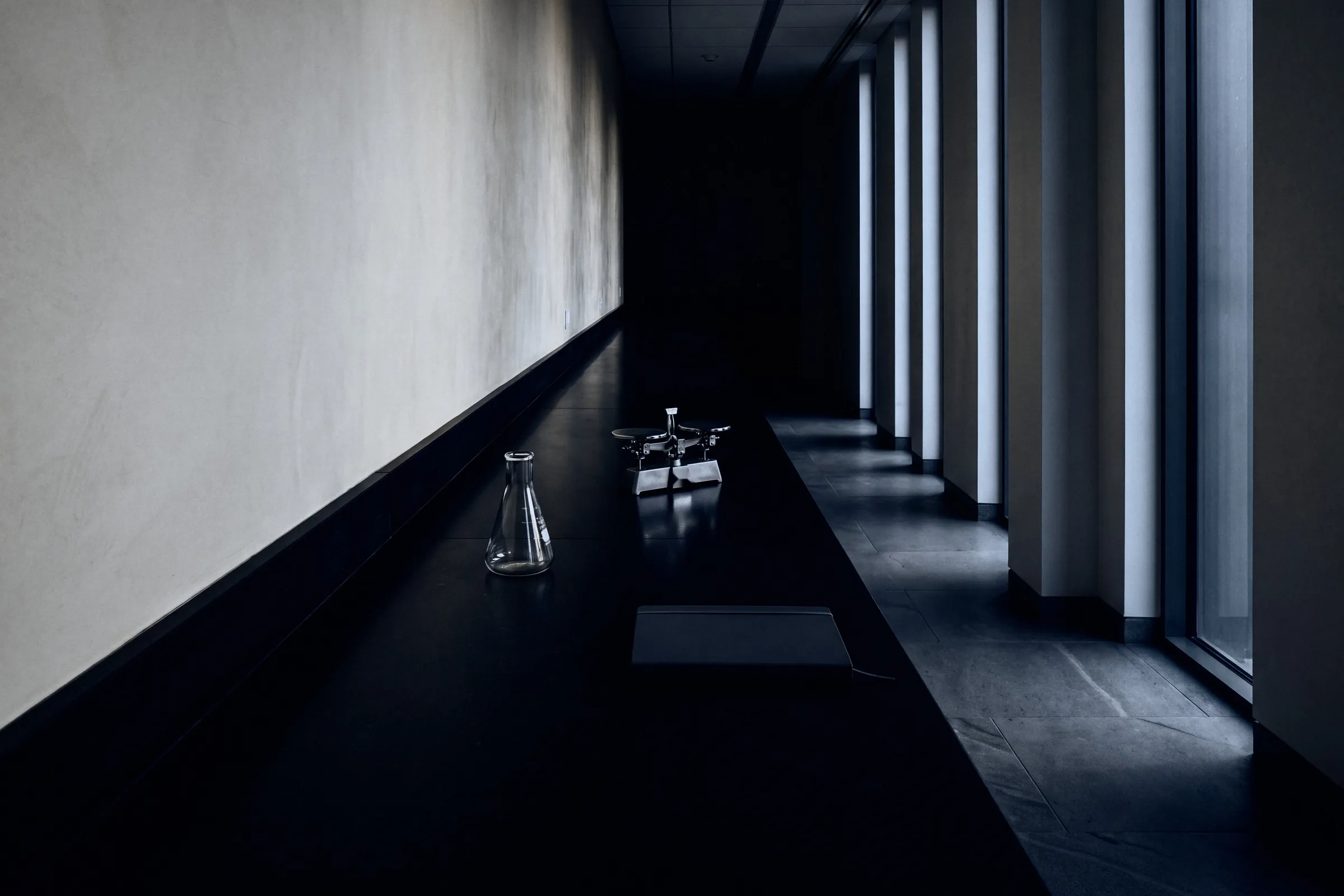 A long lab bench in a dim corridor, daylight falling through tall windows