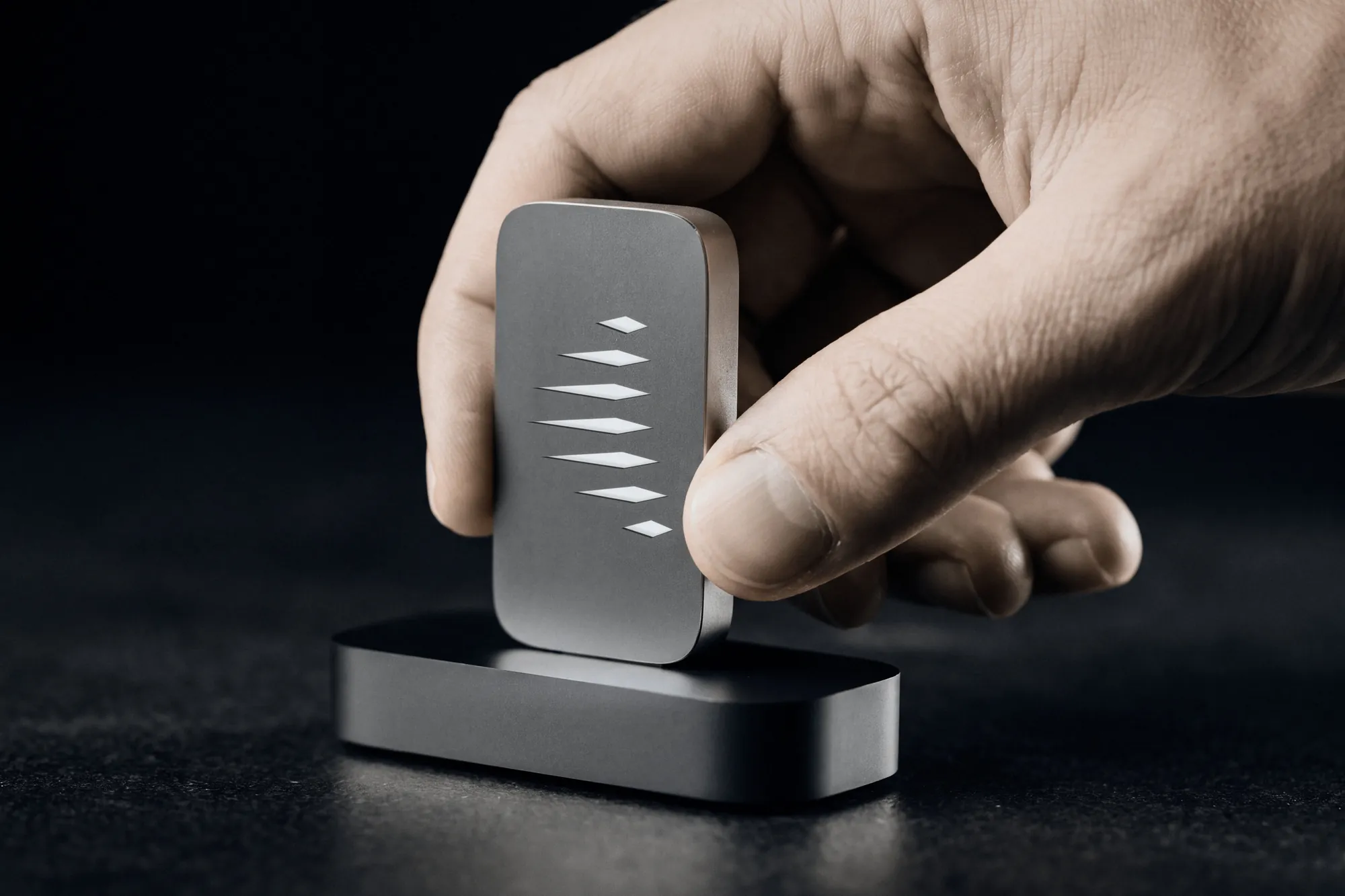 A hand setting the owner’s Key into its reader on a dark table