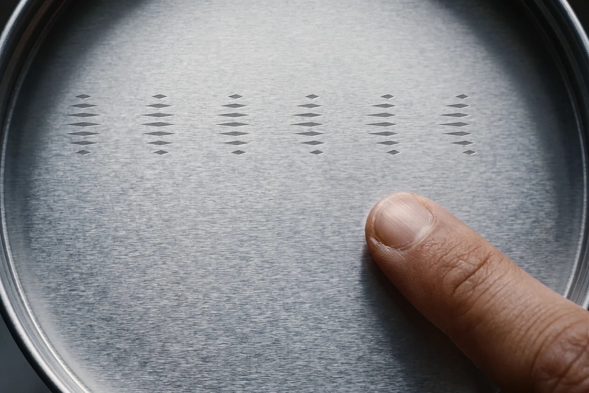 A finger tracing a row of release marks engraved in a round steel lid