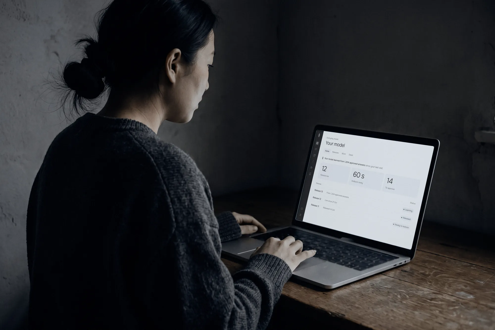 A woman at a wooden desk reviewing her model’s releases on a laptop